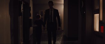 Movie still from “High-Rise” (2015), directed by Ben Wheatley – A man and a boy are walking in a dark hallway; Medium shot, Over the shoulder angle