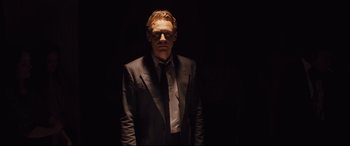 Movie still from “High-Rise” (2015), directed by Ben Wheatley – A man in a suit and tie standing in the dark; Medium shot, Low angle