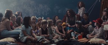Movie still from “High-Rise” (2015), directed by Ben Wheatley – A group of children sitting on the ground in front of a wall; Wide shot, High angle