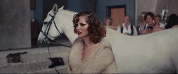 Movie still from “High-Rise” (2015), directed by Ben Wheatley – A woman in a fur coat standing in front of a white horse; Medium shot, Over the shoulder angle