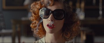 Movie still from “High-Rise” (2015), directed by Ben Wheatley – A person wearing sunglasses smoking a cigarette; Close Up shot, Over the shoulder angle
