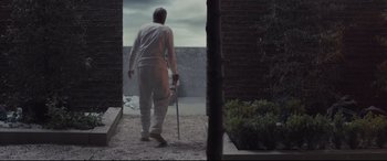 Movie still from “High-Rise” (2015), directed by Ben Wheatley – An older man walking with a cane in a courtyard; Wide shot, Low angle