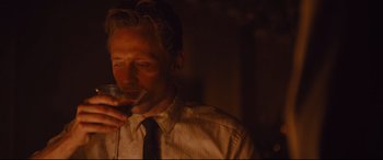 Movie still from “High-Rise” (2015), directed by Ben Wheatley – A man holding a wine glass in a dimly - lit room; Medium shot, Over the shoulder angle