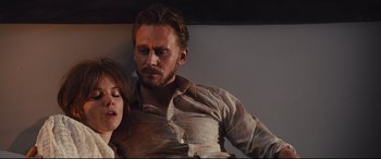 Movie still from “High-Rise” (2015), directed by Ben Wheatley – A man and a woman sitting next to each other on a couch; Medium shot, Low angle