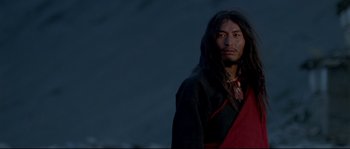 Movie still from “Himalaya” (1999), directed by Eric Valli – A man with long black hair wearing a black and red outfit; Medium shot, Low angle