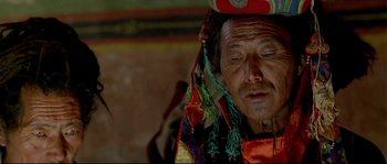 Movie still from “Himalaya” (1999), directed by Eric Valli – An old man wearing a colorful hat and looking down at the ground; Close Up shot, High angle