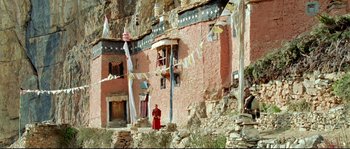 Movie still from “Himalaya” (1999), directed by Eric Valli – A person standing in front of a building with flags hanging from it; Extreme Wide shot, High angle
