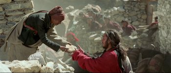 Movie still from “Himalaya” (1999), directed by Eric Valli – A man is handing bread to another man; Medium shot, Over the shoulder angle
