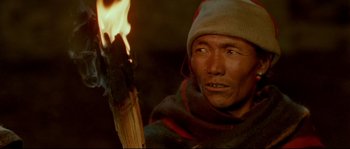 Movie still from “Himalaya” (1999), directed by Eric Valli – A man holding a stick with a flame in it; Close Up shot, High angle
