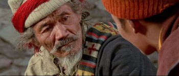 Movie still from “Himalaya” (1999), directed by Eric Valli – An old man with a beard and a red hat; Close Up shot, Over the shoulder angle