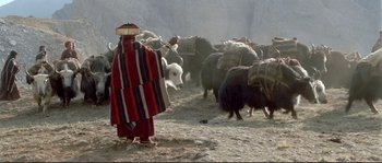 Movie still from “Himalaya” (1999), directed by Eric Valli – A man in a red and white striped robe herds a herd of sheep; Wide shot, Low angle