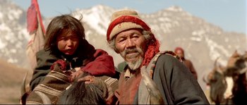 Movie still from “Himalaya” (1999), directed by Eric Valli – An old man with a beard and a red hat is smiling; Medium shot, High angle
