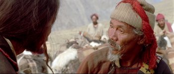 Movie still from “Himalaya” (1999), directed by Eric Valli – An old man with a beard and a hat is looking at the camera; Close Up shot, Over the shoulder angle