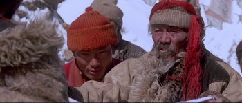 Movie still from “Himalaya” (1999), directed by Eric Valli – Two men in winter clothing and hats are holding a dog; Close Up shot, High angle