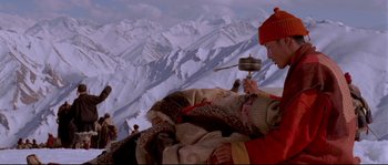 Movie still from “Himalaya” (1999), directed by Eric Valli – A person is holding a drum on a mountain top; Wide shot, Low angle