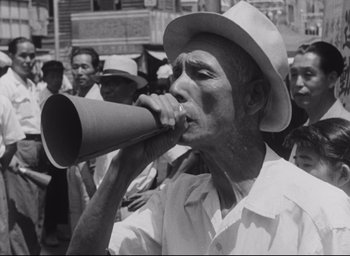 Movie still from “Hiroshima Mon Amour” (1959), directed by Alain Resnais – An older man is drinking from a paper cup; Medium shot, High angle
