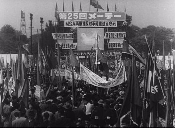 Movie still from “Hiroshima Mon Amour” (1959), directed by Alain Resnais – A crowd of people are gathered together in the street; Extreme Wide shot, High angle