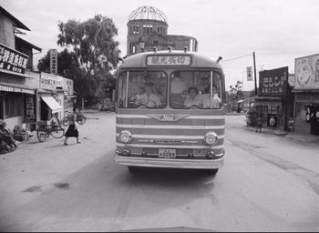 Movie still from “Hiroshima Mon Amour” (1959), directed by Alain Resnais – A bus driving down a street with people in it; Extreme Wide shot, High angle
