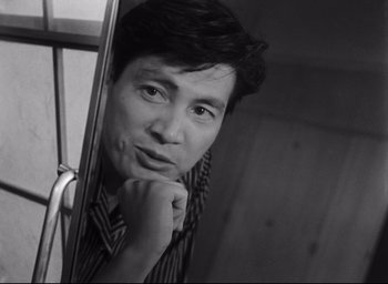 Movie still from “Hiroshima Mon Amour” (1959), directed by Alain Resnais – Black and white photograph of a man leaning against a mirror; Close Up shot, Low angle
