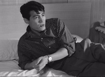 Movie still from “Hiroshima Mon Amour” (1959), directed by Alain Resnais – Black and white photograph of a man sitting on a bed; Medium shot, High angle