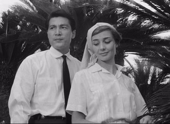 Movie still from “Hiroshima Mon Amour” (1959), directed by Alain Resnais – A man and a woman standing next to each other in front of a palm tree; Medium shot, Low angle