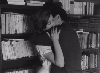 Movie still from “Hiroshima Mon Amour” (1959), directed by Alain Resnais – A man and a woman kissing in a room full of books; Medium shot, Over the shoulder angle