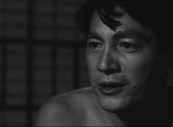 Movie still from “Hiroshima Mon Amour” (1959), directed by Alain Resnais – Black and white photograph of a shirtless man in a dimly - lit room; Close Up shot, Over the shoulder angle