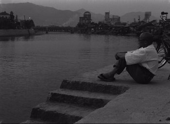 Movie still from “Hiroshima Mon Amour” (1959), directed by Alain Resnais – A man sitting on steps next to a body of water; Wide shot, High angle