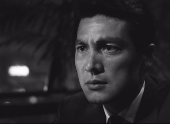 Movie still from “Hiroshima Mon Amour” (1959), directed by Alain Resnais – Black and white photograph of a man wearing a suit and tie; Close Up shot, Low angle