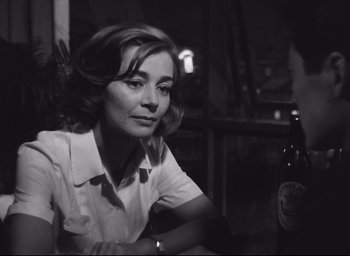 Movie still from “Hiroshima Mon Amour” (1959), directed by Alain Resnais – A black and white photo of a woman sitting in front of a bottle; Close Up shot, Over the shoulder angle