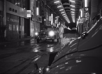 Movie still from “Hiroshima Mon Amour” (1959), directed by Alain Resnais – A couple of people standing next to a car on the street; Wide shot, High angle