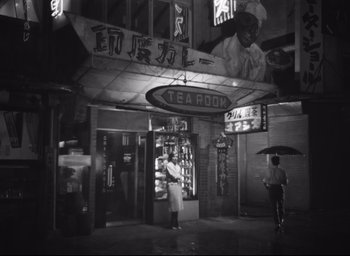 Movie still from “Hiroshima Mon Amour” (1959), directed by Alain Resnais – A black - and - white photo of a man holding an umbrella; Wide shot, Low angle
