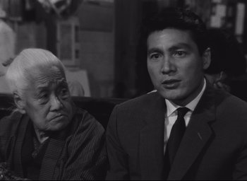 Movie still from “Hiroshima Mon Amour” (1959), directed by Alain Resnais – A man in a suit and tie sitting next to an older man; Close Up shot, Low angle