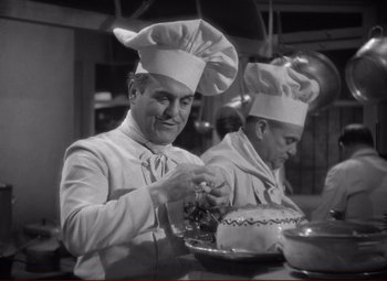 Movie still from “History Is Made at Night” (1937), directed by Frank Borzage – A man in a chef's hat is cutting a cake; Medium shot, Low angle