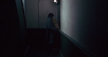 Movie still from “Unfaithful” (2002), directed by Adrian Lyne – A person holding a stack of books in a dark room; Wide shot, High angle