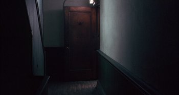Movie still from “Unfaithful” (2002), directed by Adrian Lyne – A dark room with a wooden door leading to a room with a light shining on it; Wide shot, High angle