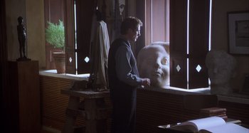 Movie still from “Unfaithful” (2002), directed by Adrian Lyne – A man standing in front of a window with a sculpture of a head; Medium shot, Over the shoulder angle