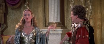 Movie still from “History of the World: Part I” (1981), directed by Mel Brooks – A woman in a gold dress holding a wine goblet in front of a man; Medium shot, Over the shoulder angle