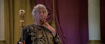 Movie still from “History of the World: Part I” (1981), directed by Mel Brooks – An older man wearing a crown smoking a cigarette; Close Up shot, Over the shoulder angle