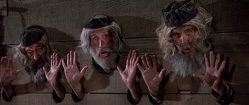 Movie still from “History of the World: Part I” (1981), directed by Mel Brooks – A group of three men wearing hats and one is holding his hand up to his face; Medium shot, Low angle