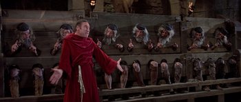 Movie still from “History of the World: Part I” (1981), directed by Mel Brooks – A man dressed in a monk's robe and holding his hand out to a group of people; Wide shot, Over the shoulder angle