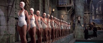 Movie still from “History of the World: Part I” (1981), directed by Mel Brooks – A line of women in bathing suits are lined up in front of a stone wall; Wide shot, Low angle