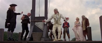 Movie still from “History of the World: Part I” (1981), directed by Mel Brooks – A man in a white outfit standing next to a guillotine; Wide shot, Low angle