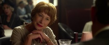 Movie still from “Hitchcock” (2012), directed by Sacha Gervasi – An older woman sitting at a table with a glass; Close Up shot, Over the shoulder angle