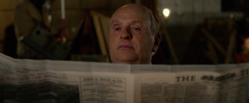 Movie still from “Hitchcock” (2012), directed by Sacha Gervasi – An older man reading a newspaper in a dark room; Close Up shot, Over the shoulder angle