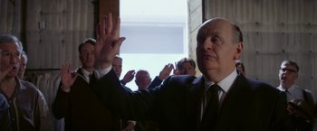 Movie still from “Hitchcock” (2012), directed by Sacha Gervasi – A man in a suit and tie raising his hands; Close Up shot, Low angle