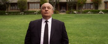 Movie still from “Hitchcock” (2012), directed by Sacha Gervasi – A man in a suit and tie standing in front of a house; Medium shot, Low angle