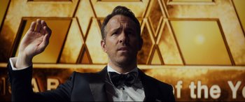 Movie still from “Hitman's Wife's Bodyguard” (2021), directed by Patrick Hughes – A person wearing a suit and bow tie; Close Up shot, Over the shoulder angle