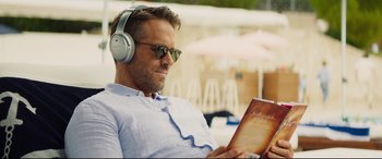 Movie still from “Hitman's Wife's Bodyguard” (2021), directed by Patrick Hughes – A man wearing headphones and reading a book; Close Up shot, High angle
