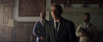 Movie still from “Hitman's Wife's Bodyguard” (2021), directed by Patrick Hughes – A man in a suit standing next to another man in a suit; Medium shot, Low angle